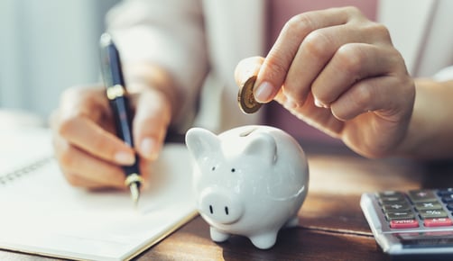 person calculating costs and putting coin in piggy bank